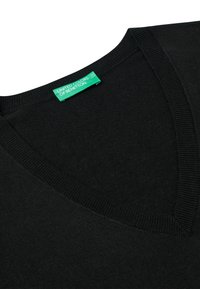 Černý svetr s výstřihem do V a žebrovaným límcem. Materiál vypadá jemně a hladce. Zelená visačka nese nápis "UNited Colors of Benetton."