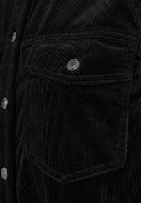 Svart korduroy-skjorta med silverfärgade metallknappar och två bröstfickor med klaffar, som visar en räfflad textur och ren sömnad.