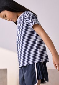 T-shirt en coton rayé bleu marine et blanc, à manches courtes et col rond. Associé à un short plissé bleu marine avec des accents blancs.
