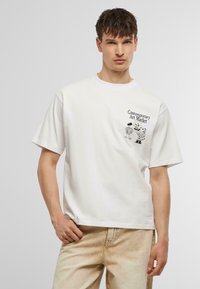 Witte katoenen t-shirt met ronde hals, voorzien van een grafische print van een persoon en een koe. Korte mouwen, relaxte fit, subtiele textuur.