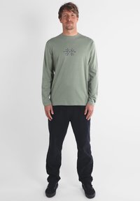 Chemise en coton vert clair à manches longues avec un design brodé au centre. Associée à un pantalon bleu marine foncé et des baskets noires.
