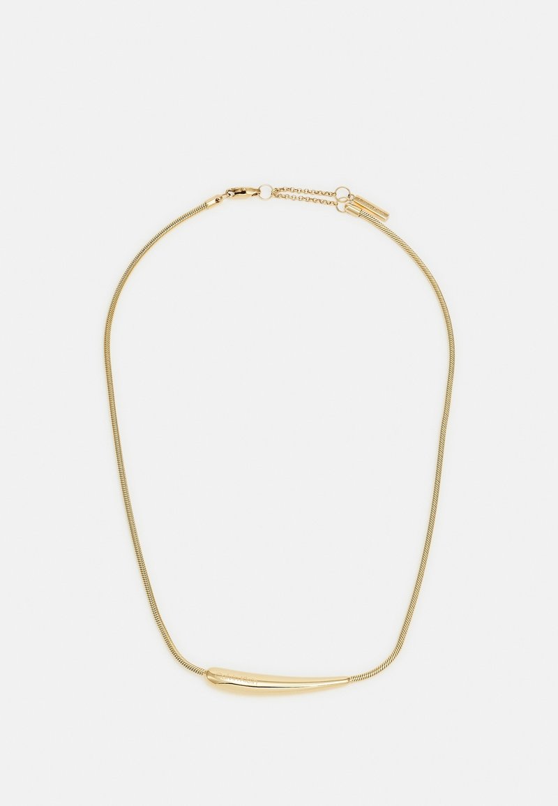 Collier délicat en chaîne d'or avec un pendentif barre en or lisse légèrement incurvé et un petit fermoir réglable sur fond blanc.