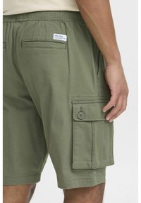 Pantaloni scurți cargo verzi, fabricati dintr-un material ușor. Au o talie elastică, buzunare laterale și un buzunar cargo cu buton pe coapsă.