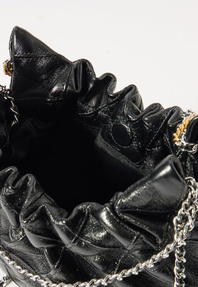 Mustan nahkakäsilaukku rypistettynä ylhäältä, jossa on metalliketjuasuste. Sisus on sileä ja vuoriton, tarjoten avaran aukon.