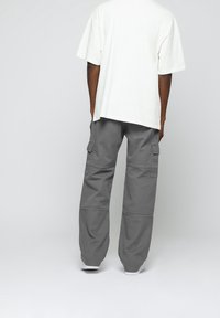 Grijze cargo broek met grote zijzakken, gecombineerd met een losse, witte katoenen t-shirt. Soepele textuur en relaxte silhouet.