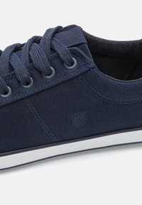 Baskets en toile navy avec lacets foncés, bout rond et semelle en caoutchouc blanc. Dispose d'un dessus texturé et d'un logo sur le côté.