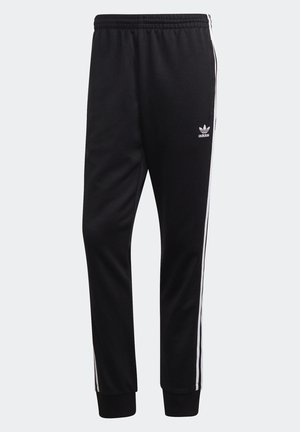 Pantalon de survêtement noir Adidas avec des bandes blanches sur les côtés, taille élastique, chevilles resserrées et logo trèfle Adidas sur la cuisse gauche.