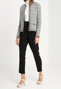 Tweedjacka i svart och vitt med en kragslös design, i kombination med svarta skräddarsydda byxor och vita blockklacksandaler.