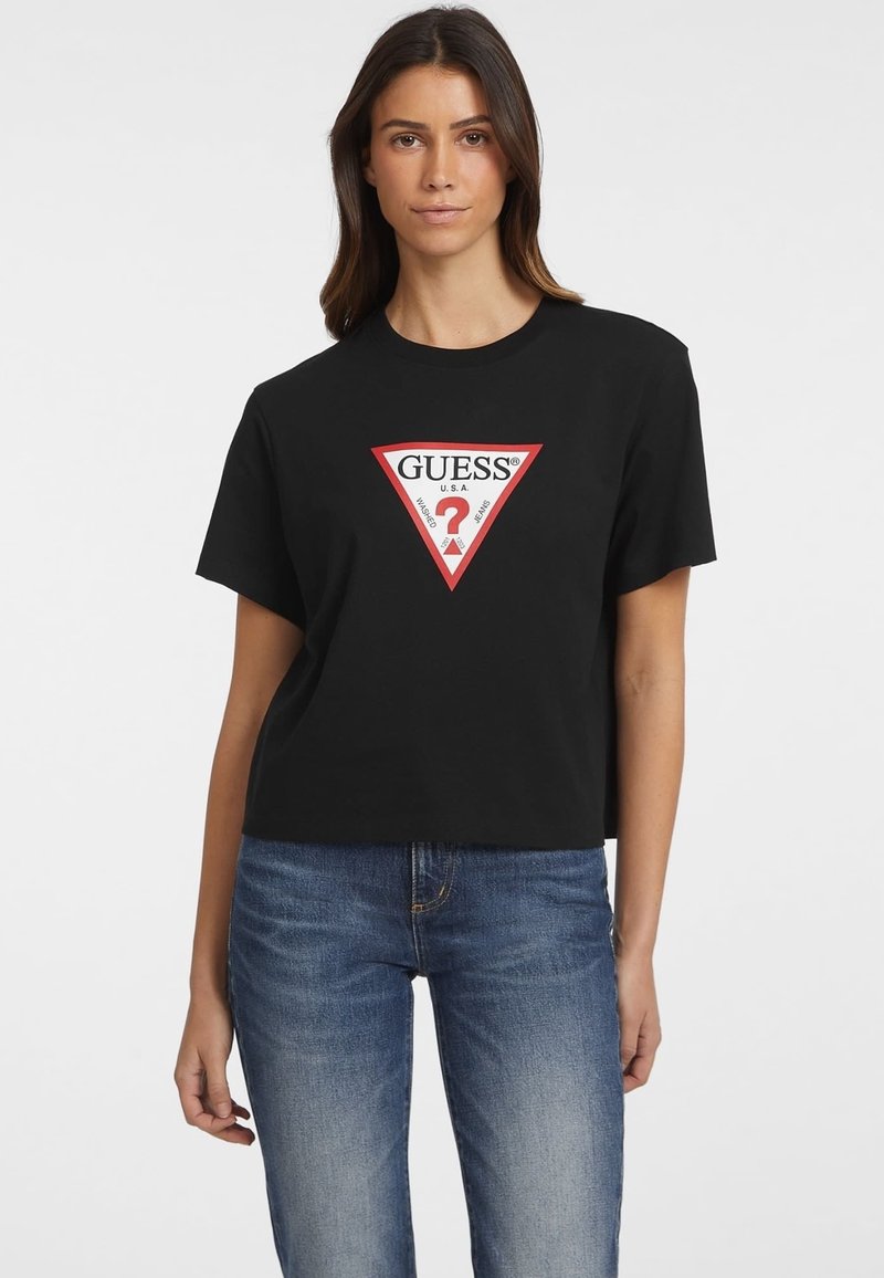 T-shirt en coton noir avec un logo triangulaire rouge et un texte blanc, à manches courtes et à coupe décontractée, associé à un jean en denim bleu.