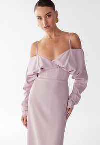 Dlouhý rukáv, šaty s odhalenými rameny v světle levandulové barvě. Mají drapovaný živůtek, obepnutý pas a hladkou texturu s minimálními detaily.
