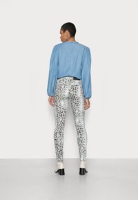 Blusa azul de mangas longas com ombros bufantes, combinada com leggings justas com estampa de cobra em branco e cinza, e botins de salto bege.