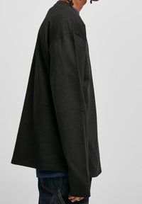 Long-sleeve black shirt in a soft fabric; loose fit with dropped shoulders and extended sleeves. Features a visible inner layer of blue.