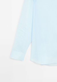 Camicia a manica lunga azzurro chiaro realizzata in un tessuto morbido; presenta una manica con polsino e un orlo leggermente curvo. Design minimalista, senza motivi.