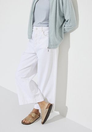 Veste zippée texturée bleu clair, haut gris, pantalon large blanc et sandales beiges avec deux boucles et semelle texturée.