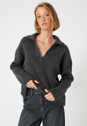 Pull gris foncé à col en V avec un design texturé à côtes. Il a des manches longues et une coupe décontractée. Assorti avec un jean noir.
