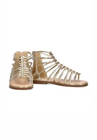Sandalias gladiadoras metálicas doradas con múltiples correas, diseño de punta abierta, suela plana y una textura suave. Cuenta con un tacón trasero para mayor soporte.