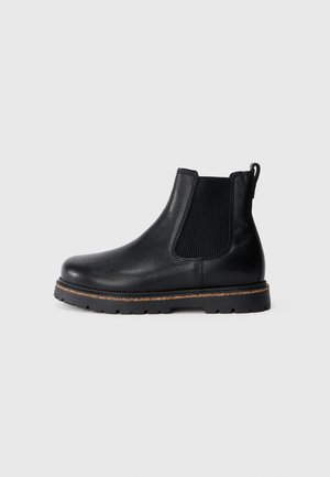 Botas Chelsea de cuero negro con paneles laterales elásticos, puntera redondeada y suela texturizada. Cuenta con una lengüeta en la parte trasera para facilitar su colocación.