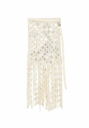 Sukňa v krémovej farbe s kruhovým vzorom vystrihnutých otvorov, kovovými reflexnými diskami, dlhými visiaci slučkami a pripevneným bočným remienkom s prackou.