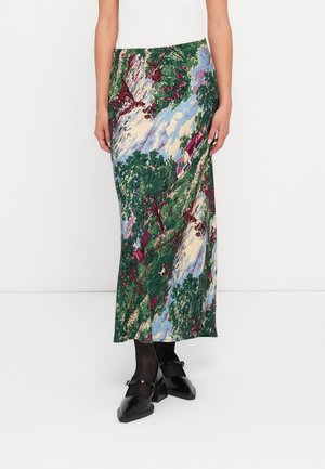 Jupe avec imprimé scénique vert, bleu, crème et bordeaux avec des arbres et des maisons, portée avec des collants noirs et des chaussures Mary Jane noires.