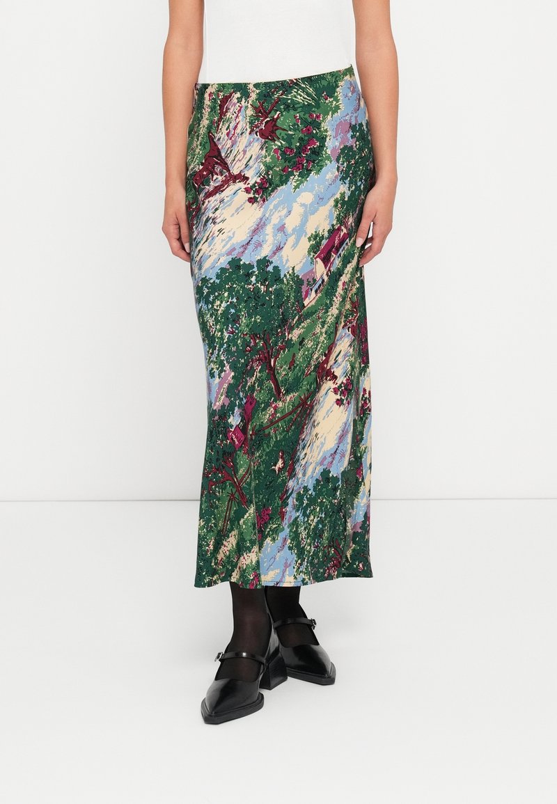 Jupe avec imprimé scénique vert, bleu, crème et bordeaux avec des arbres et des maisons, portée avec des collants noirs et des chaussures Mary Jane noires.
