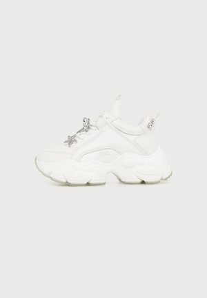 Λευκό chunky sneaker με παχιά σόλα και ασημένιο γούρι σε σχήμα αστέρι στα κορδόνια, σε ανοιχτό φόντο.