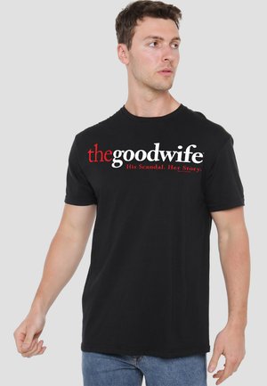 Black cotton t-shirt featuring "thegoodwife" logo in white and red, with the tagline "His Scandal. Her Story." in a bold, prominent design.