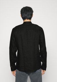 Camicia a maniche lunghe nera in lino con colletto, polsini abbottonati e vestibilità comoda. Tessuto leggermente testurizzato e fessure laterali sull'orlo per maggiore comodità.