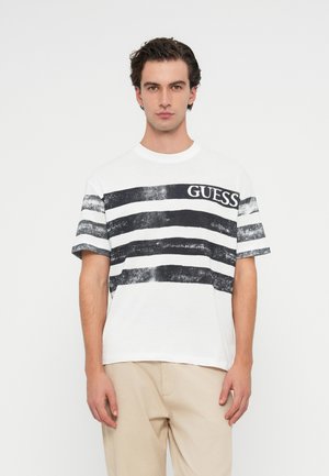 Weiße Baumwoll-T-Shirt mit kräftigen schwarzen horizontalen Streifen und dem "GUESS"-Logo auf der Vorderseite. Kurze Ärmel und lockere Passform.
