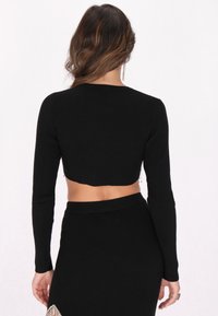 Fekete bordázott crop top hosszú ujjakkal és lekerekített dekoltázzsal, mely texturált anyagból készült és rövid hátkivágással rendelkezik.