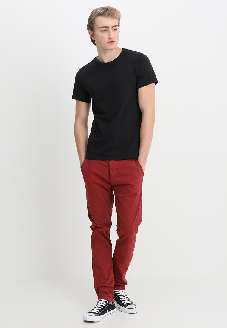 Camiseta de algodón negra, ajustada, combinada con chinos rojos, diseño de pierna recta, y zapatillas negras y blancas con textura de lona y suela de goma.