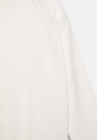 Fehér, texturált pulóver, lágy, kötött anyaggal, enyhén emelt gallérral és lelógó vállakkal, kiemelve a varrás nélküli kialakítást.