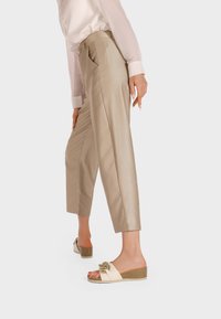 Pantaloni beige a vita alta con dettagli a cucitura verticale, abbinati a sandali scivolati color crema chiaro con fasce testurizzate e un fiocco decorativo.