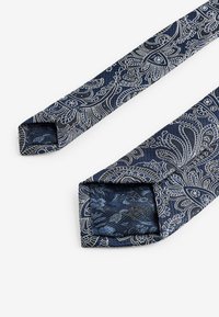 Cravata bleu marin cu un model floral paisley alb, detaliat, dintr-un material texturat, cu vârfuri pătrate. Prezintă o finisare netedă și o formă îngustă.
