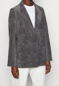 Blazer in velluto a coste grigio con rever a punta, chiusura a un bottone e due tasche frontali. Il tessuto presenta un motivo rigato testurizzato.
