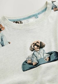 Felpa grigia chiara a maniche lunghe con un cane dei cartoni animati in pigiama a righe blu, seduto su un cuscino, con una texture morbida e colletto a coste.