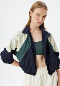 Värgblookerad jacka i marinblått, krämfärgat och grönt; lättviktsmaterial; dragkedja framtill; elastiska muddkanter och fåll; meshinredning.