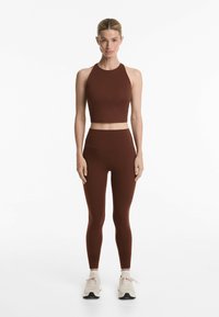 Set de îmbrăcăminte sport burgund cu un top scurt fără mâneci și colanți cu talie înaltă, dintr-un material neted, texturat. Pantofi de sport de culoare deschisă.