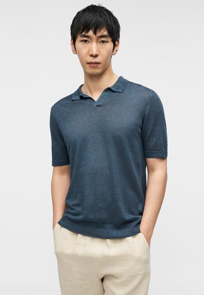 Blå kortermet poloshirt med lett v-formet hals, laget av lett teksturert stoff. Har myk krage og tettsittende kant.