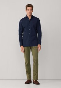 Camisa azul marino abotonada con mangas largas, diseño entallado. Combinada con pantalones verde oliva y mocasines marrones. Textura suave, estilo clásico.