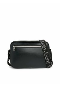 Borsa a tracolla nera in pelle con zip argento, tracolla regolabile con testo "Calvin Klein Jeans", forma rettangolare elegante, texture liscia.