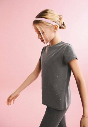 Sivá tričko s krátkymi rukávmi so malými dekoračnými cvočkami, doplnené o zodpovedajúce sivé legíny, na ružovom pozadí. Hladká textúra látky.