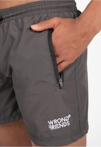 Grijze zwemshorts met een elastische tailleband en een zijzak met rits. Heeft een wit geborduurd logo op het onderbeen. Lichtgewicht materiaal.