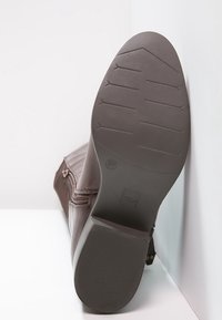 Botín marrón con suela de goma plana, fondo texturizado para agarre, cremallera lateral y detalles cosidos. Etiqueta de tamaño visible: 37.