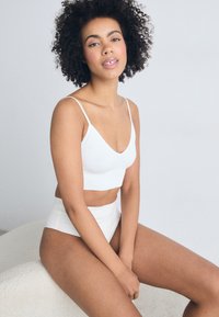 Wit geribbeld crop top met verstelbare bandjes, gecombineerd met hoge witte slipjes. Gladde textuur, minimalistisch ontwerp en neutrale kleuren.