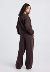 Brown sweatshirt and matching pants, featuring a relaxed fit, soft texture, and a simple design with minimal accents and side stripes.