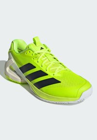 Chaussure de sport jaune néon avec des rayures noires, tige en maille, col rembourré et semelle blanche avec un motif de grip texturé.