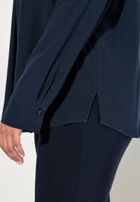 Maglia a manica lunga blu navy realizzata in tessuto leggero, con una fessura laterale e polsini bottonati, abbinata a pantaloni blu navy coordinati.