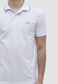 Polo bianco realizzato in cotone, con colletto e maniche corte. Accenti blu sui polsini e un piccolo logo sul petto.