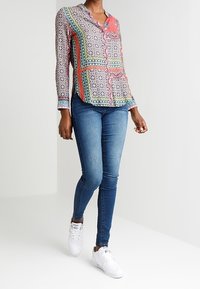Multicolored patterned button-up shirt with collar and long sleeves, paired with blue skinny jeans and white sneakers.