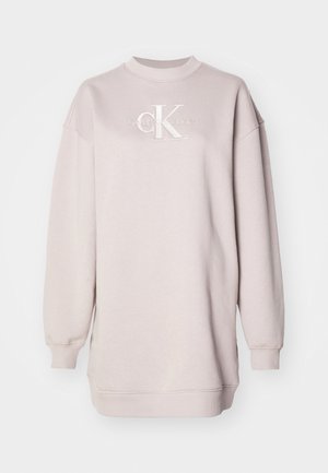 Gai bēšs treniņjakas krekls ar apaļu kakla izgriezumu, pārāk liels, ribinātas piedurknes un izšūts "CK" logo priekšpusē. Gluda, mīksta auduma tekstūra.